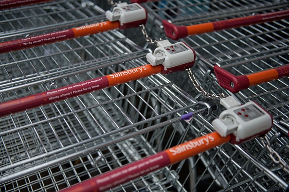 The logos of supermarket chain Sainsbury's are pictured on the handles of shopping trolleys outside a store in Stockport, northern England on April 30, 2018. - Britain's second and third biggest supermarket chains Sainsbury's and Walmart-owned Asda have agreed to merge, the pair said Monday, hoping to create a £13-billion ($18-billion, 15-billion-euro) retail king and leapfrog UK number one Tesco. The blockbuster deal -- which is effectively a takeover bid with Sainsbury's acquiring a majority 58-percent stake -- comes as the British supermarket sector faces squeezed profit margins and fierce competition from German-owned discounters Aldi and Lidl and online US titan Amazon. (Photo by OLI SCARFF / AFP) (Photo credit should read OLI SCARFF/AFP/Getty Images)
