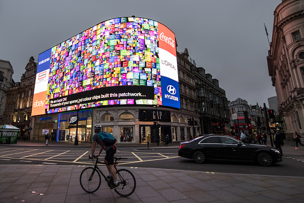 LONDON, ENGLAND - OCTOBER 26: Members of the public watch as an animation is seen after the countdown as the Piccadilly Circus lights are switched back on after a nine month renovation on October 26, 2017 in London, England. The new Piccadilly Circus lights advertising boards replace a patchwork of screens with a single 4K LED digital screen, the largest of its kind in Europe. (Photo by Chris J Ratcliffe/Getty Images)