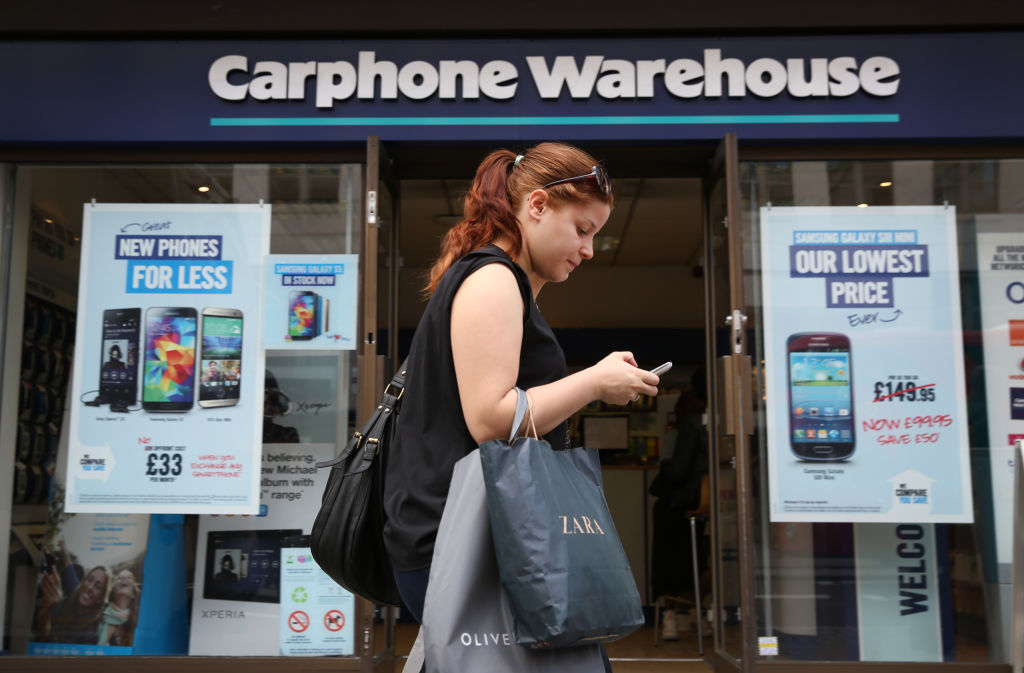 LONDON, ENGLAND - MAY 15:  A shopper uses her mobile phone as she walks past a branch of Carphone Warehouse on May 15, 2014 in London, England. Dixons Retail, the parent group of PC World and Currys have announced  a £3.8 bn merger with mobile phone retailer Carphone Warehouse.  (Photo by Peter Macdiarmid/Getty Images)