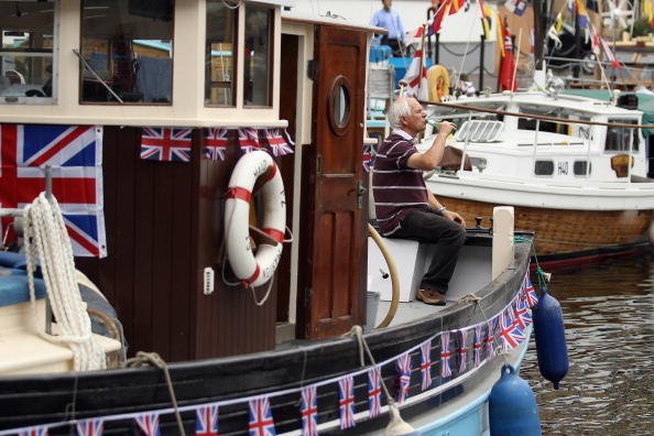 LONDON, ENGLAND - JUNE 01:  A man sits on a boat at South Quay, where many of the boats taking part in the Queen's Diamond Jubilee River Pageant are moored on June 1, 2012 in London, England. With two days to go before the start of Diamond Jubilee celebrations final preparations are taking place in the capital.  (Photo by Dan Kitwood/Getty Images)