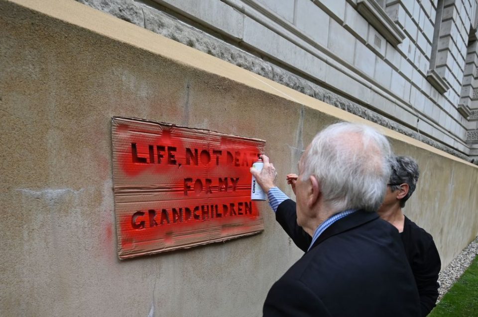 A couple of climate change activists including Phil Kingston (L), 83, from the group Extinction Rebellion spray paint using a stencil a message that reads "Life, not death for my grandchildren" on the side of the building housing the Treasury in central London, on October 7, 2019 as part of the group's global climate protests. - Extinction Rebellion has scheduled non-violent protests chiefly in Europe, North America and Australia over the next fortnight. (Photo by Ben STANSALL / AFP) (Photo by BEN STANSALL/AFP via Getty Images)