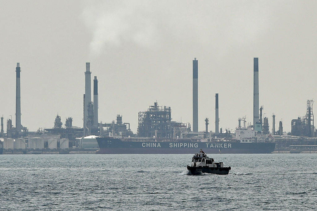 A boat (foreground) is seen past an oil tanker (background) docked next to an oil refinery on Bukom island off Singapore.