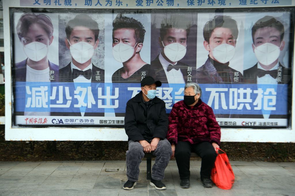 A man and woman sit in front of a poster reminding citizens to wear face masks as a preventive measure against the COVID-19 coronavirus, at a bus stop in Bozhou, in China's eastern Anhui province on March 6, 2020. - China reported 30 more deaths from the new coronavirus outbreak on March 6, with fresh infections rising for a second straight day and 16 new cases imported from overseas. (Photo by STR / AFP) / China OUT (Photo by STR/AFP via Getty Images)