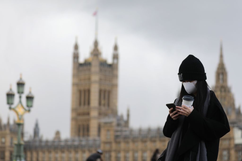 A pedestrian wearing a face mask walks along Westminster Bridge in front of the Houses of Parliament