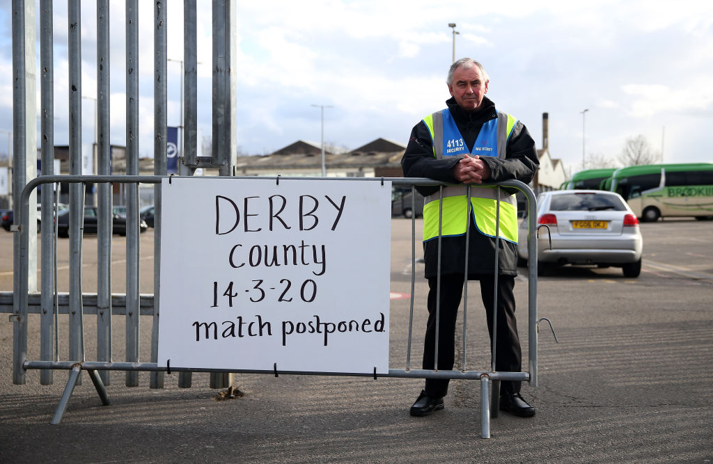 A steward next to a postponement notice at Derby County