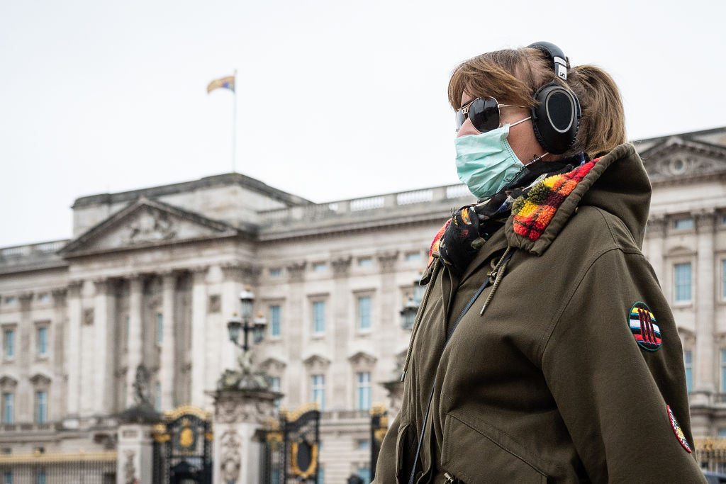 woman wearing a face mask walks past Buckingham Palace