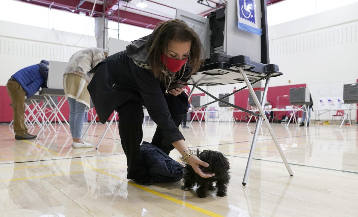 A voter stops her dog from barking as she fills in her ballot at Greenwich High School in Greenwich, Connecticut 
