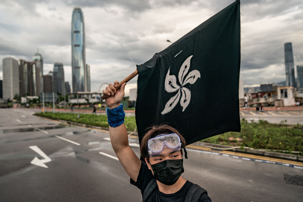 HONG KONG, HONG KONG - JULY 1:  An anti-extradition protester waves a black flag on a street outside the Legislative Council Complex ahead of the annual flag raising ceremony of 22nd anniversary of the city's handover from Britain to China on July 1, 2019 in Hong Kong, China. Pro-democracy demonstrators in Hong Kong have organized rallies over the past weeks, calling for the withdrawal of a controversial extradition bill, the resignation of the territory's chief executive Carrie Lam, an investigation into police brutality, and drop riot charges against peaceful protesters. (Photo by Anthony Kwan/Getty Images)