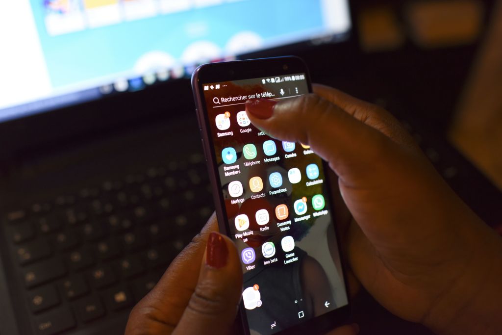A woman uses a smartphone in front of a laptop on April 3, 2019, in Abidjan. - According to the figures of the platform of the fight against cybercrime (PLCC) of the national police, nearly one hundred crooks of the internet, were arrested in 2018 in Ivory Coast, a country known for its scammers on the web, has announced on April 2, 2019 the Ivorian authority of regulation of the telephony. (Photo by ISSOUF SANOGO / AFP) (Photo credit should read ISSOUF SANOGO/AFP/Getty Images)
