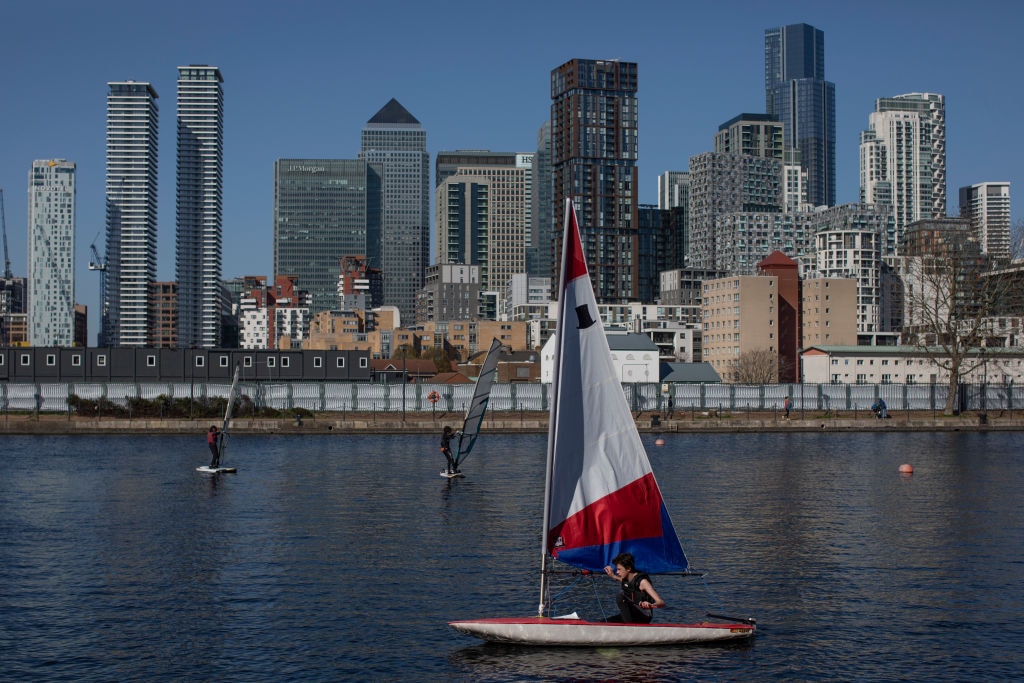 LONDON, UNITED KINGDOM - MARCH 29: A young man sails beneath the Canary Wharf skyline from the Docklands sailing and watersports centre on March 29, 2021 in London, United Kingdom. Today the government eased its rules restricting outdoor socialising and sport in England, the first milestone on the government's "roadmap" out of the Covid-19 lockdown measures imposed in December. Groups of either six people or two households can meet outside and organised outdoor sport is allowed to resume. (Photo by Dan Kitwood/Getty Images)