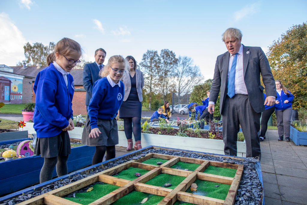 CRUMLIN, NORTHERN IRELAND - OCTOBER 21: Britain's Prime Minister Boris Johnson (R) joins schoolchildren playing a game of Tic Tac Toe in their sensory garden (which he wins) during a visit to Crumlin Intergrated primary school after attending a service to mark the centenary of the creation of Northern Ireland after the partition of Ireland, on October 21, 2021 in County Antrim, Northern Ireland. (Photo by Paul Faith - WPA Pool/Getty Images)