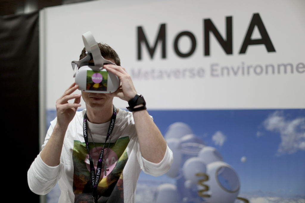 MIAMI, FLORIDA - DECEMBER 01: Matthew Hoerl of MoNA Gallery wears a VR headset as he speaks with attendees at their booth during the DCentral Miami Conference at the Miami Airport Convention Centre on December 01, 2021 in Miami, Florida. MoNA Gallery describes itself as seeding the open metaverse through the creation and use of unique 3D spaces. Organizers say this is the largest in-person combined NFT and DeFi conference in history. (Photo by Joe Raedle/Getty Images)