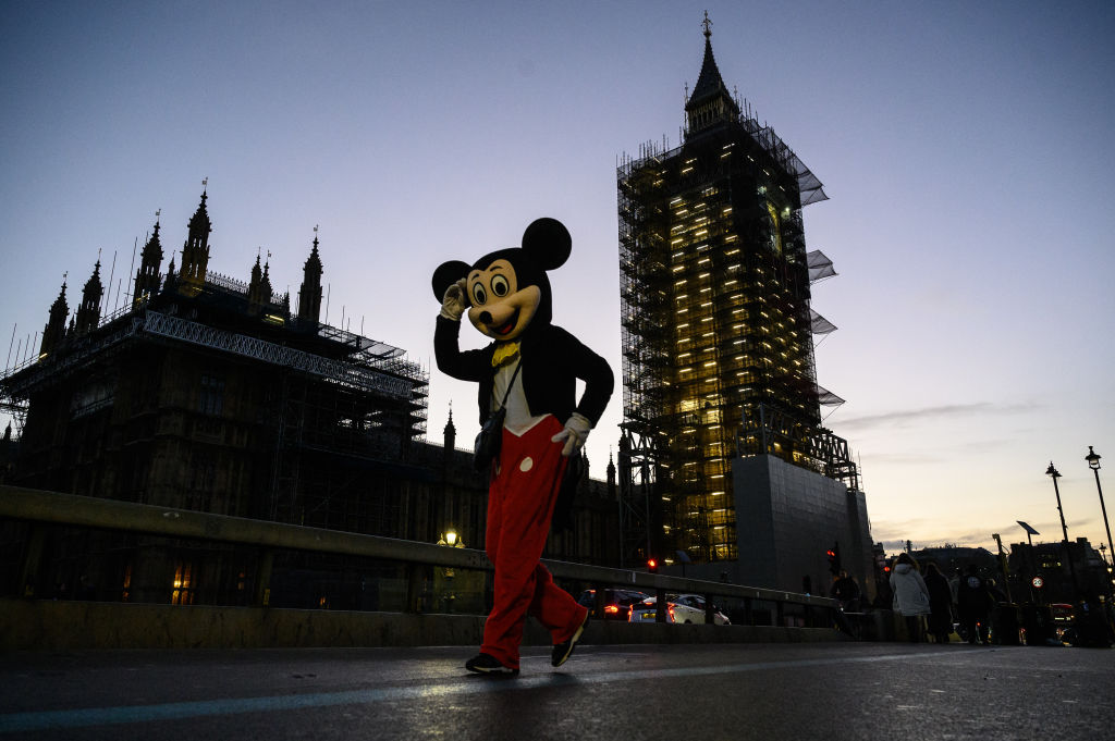 LONDON, ENGLAND - DECEMBER 11: A street performer dressed as Mickey Mouse greets tourists as the sun sets over the Houses of Parliament on December 11, 2020 in London, England. The trade deal negotiations between the EU and the UK have reached an impasse with negotiators stuck on two points: a so-called level playing field to ensure fair competition between companies and fishing quotas. Negotiators from both sides have until Sunday to reach a deal or the UK will leave the EU with no deal and will begin trading on WTO terms. (Photo by Leon Neal/Getty Images)