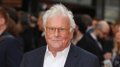 Richard Eyre, stage and film director, with white hair and orange glasses, wearing a dark suit and white shirt.