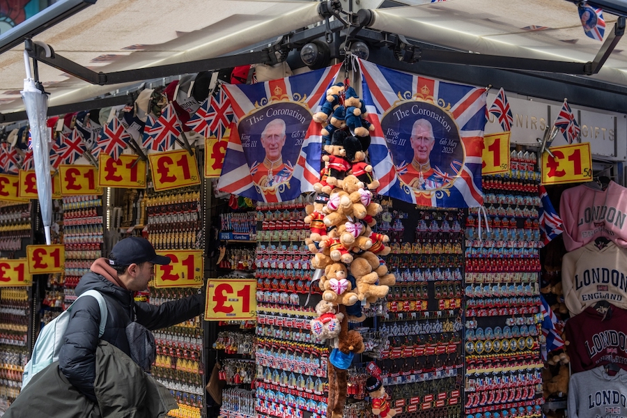 A man looks at items on display at a souvenir stand as King Charles III Coronation flags are displayed above him on April 24, 2023 in London, England. The Coronation of King Charles III and The Queen Consort will take place on May 6, part of a three-day celebration. (Photo by Carl Court/Getty Images)