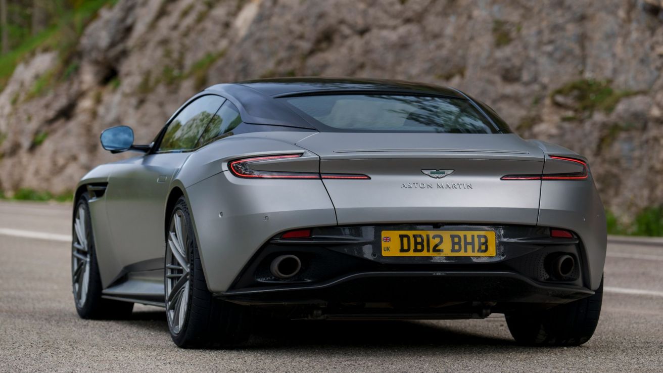 Aston Martin losses halved in its full-year results despite a hit to wholesale volumes after production issues with the roll-out of its DB12 model.