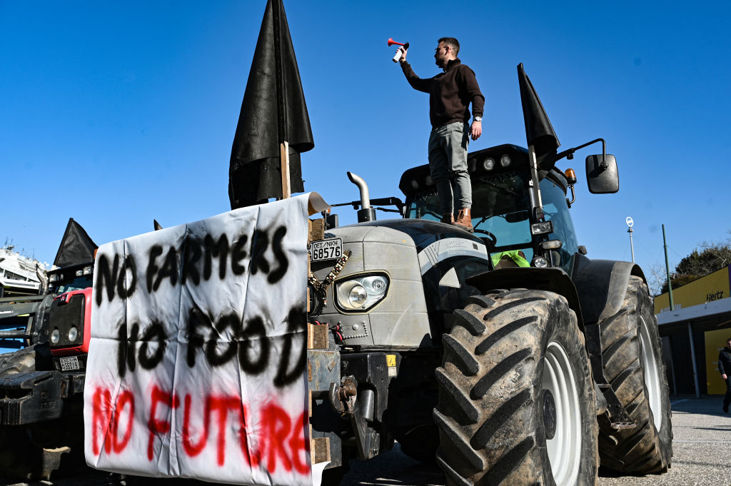 A man stands on his tractor as farmers gather, with their tractors, at the Agrotica agricultural fair in Thessaloniki on February 1, 2024, as they protest against rising operation and production costs, while also demanding better compensation for crop losses due to natural disasters and disease, as well as the construction of infrastructure to protect agriculture from extreme weather conditions. (Photo by Sakis MITROLIDIS / AFP) (Photo by SAKIS MITROLIDIS/AFP via Getty Images)