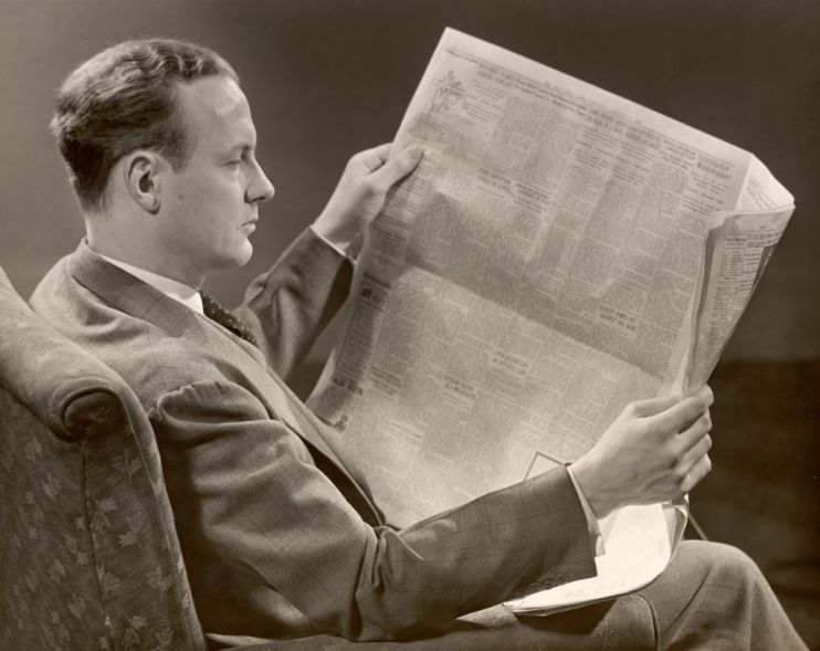A man in a suit sits in a chair and reads a newspaper which he holds in his hands, New York state, 1930s. (Photo by George Marks/Retrofile/Getty Images)
