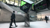 London Stock Exchange interior with a digital display showing LON.STK.EXCH and traders walking past.