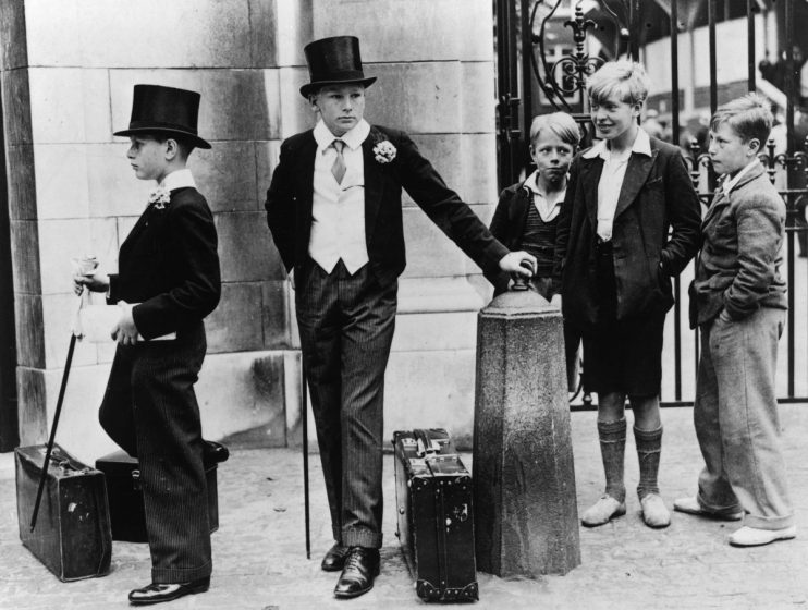 A group of local boys look on with curiosity and amusement at Harrow schoolboys Peter Wagner (left) and Thomas Dyson in their formal uniform at the Eton vs Harrow cricket match on 9 July 1937 at the Lord's cricket ground, London. (Photo by Jimmy Sime/Central Press/Hulton Archive/Getty Images)