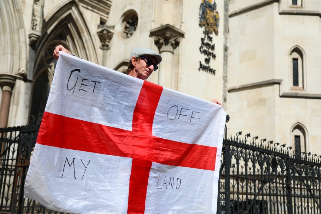 LONDON, ENGLAND - AUGUST 29: A protester holds the flag of St George with the words "Get of my land" outside the Court of Appeal ruling on housing migrants at The Bell Hotel in Epping at the Royal Courts of Justice on August 29, 2025 in London, England. This afternoon the Court of Appeal rules on whether to overturn a temporary injunction to block asylum seekers from being housed at the Bell Hotel in Epping. (Photo by Alishia Abodunde/Getty Images)