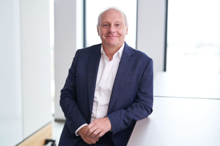 Business meeting in modern office with diverse team discussing strategy and reviewing financial charts on digital screen.