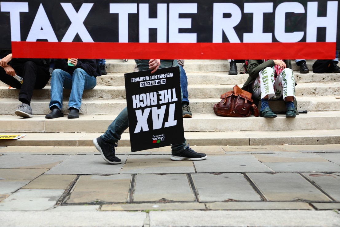 LONDON, ENGLAND - JUNE 7: A person walks behind a banner with a placard that reads 'Tax The Rich' during preparations ahead of a protest over benefits cuts organised by People's Assembly on June 7, 2025 in London, England. Activists as well as some Labour MPs have objected to the government's proposed benefits cuts, including tightened criteria for personal independence payments (Pip) for people with disabilities. (Photo by Alishia Abodunde/Getty Images)
