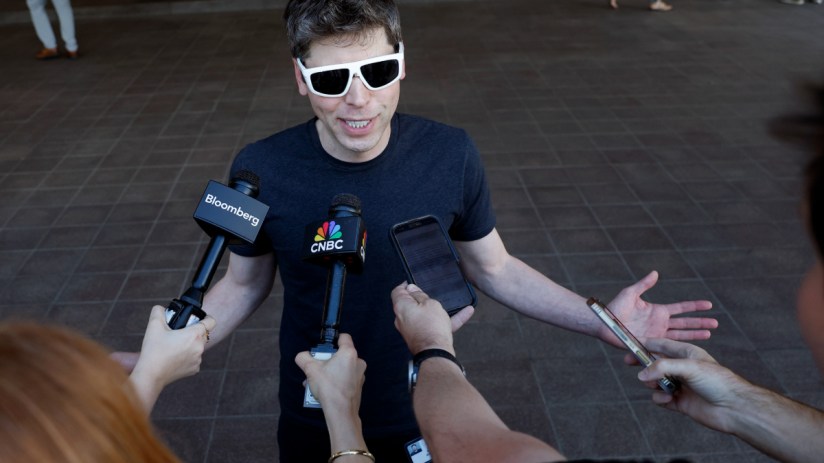 Sam Altman discussing AI advancements at a tech conference podium, wearing a suit, with a large audience in the background.