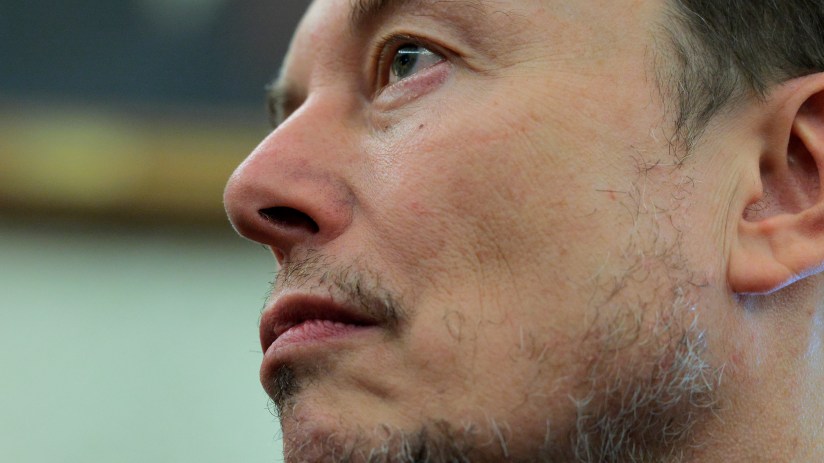 Elon Musk speaking at a business conference, wearing a suit, with a digital backdrop showcasing futuristic technology elem...