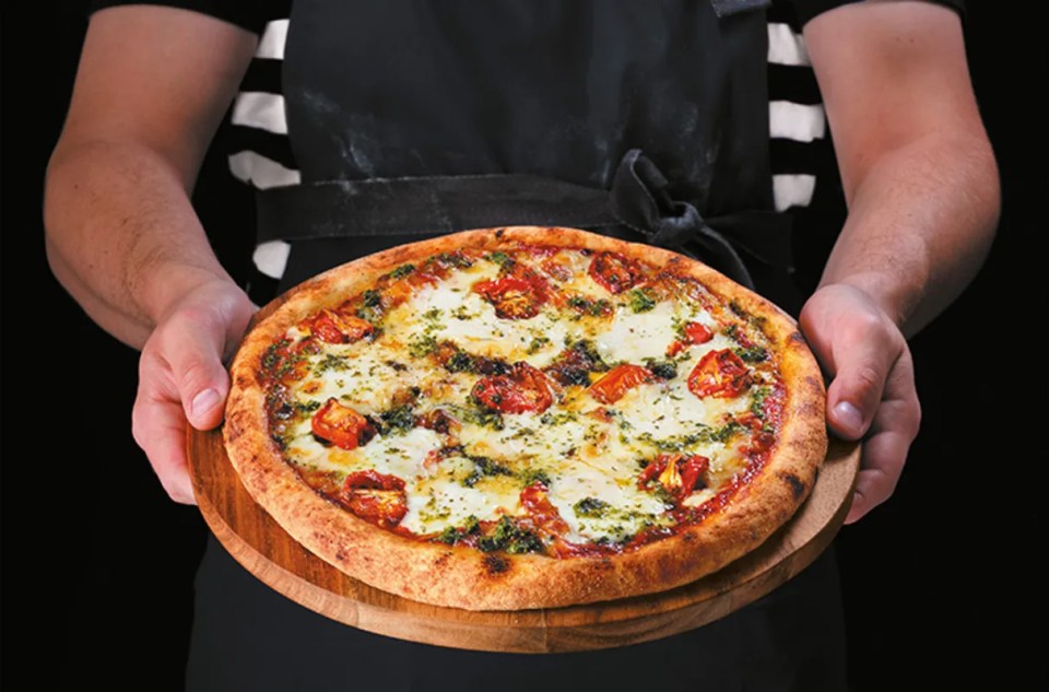PizzaExpress pizzaiolo crafting Margherita Speciale pizza with fresh ingredients in a bustling kitchen setting