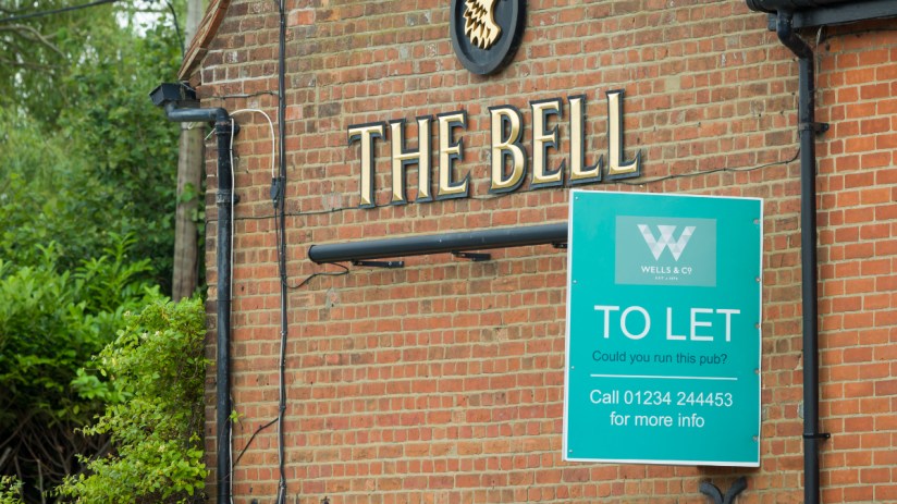 Exterior view of closed pub with boarded windows, sign indicating permanent closure, and empty outdoor seating area