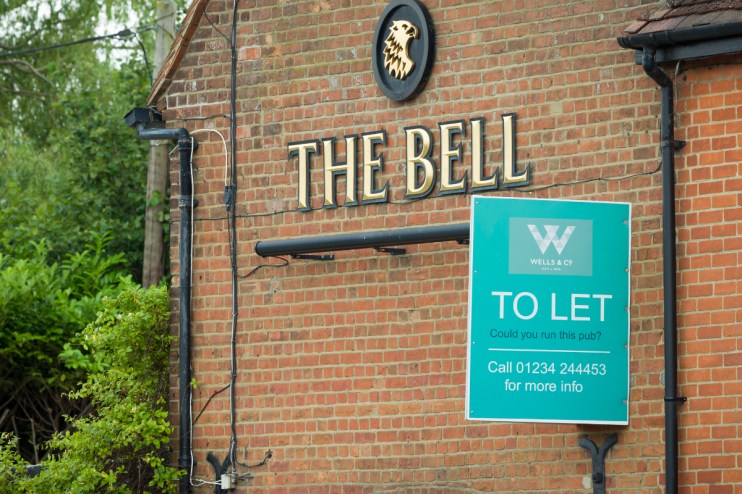 Exterior view of closed pub with boarded windows, sign indicating permanent closure, and empty outdoor seating area
