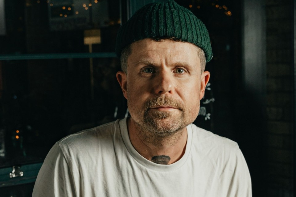 Robin Gill delivering a news report on a general topic, wearing a professional suit, with a newsroom backdrop.