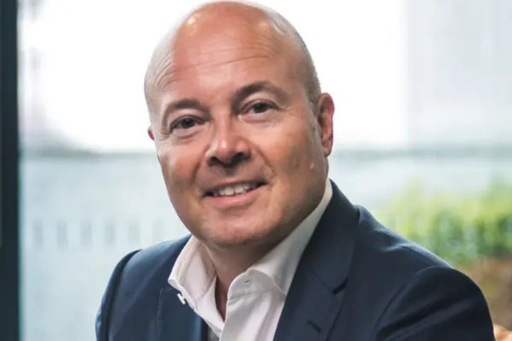 Steven Fine discussing a business strategy at a conference, wearing a suit and gesturing towards a presentation slide.