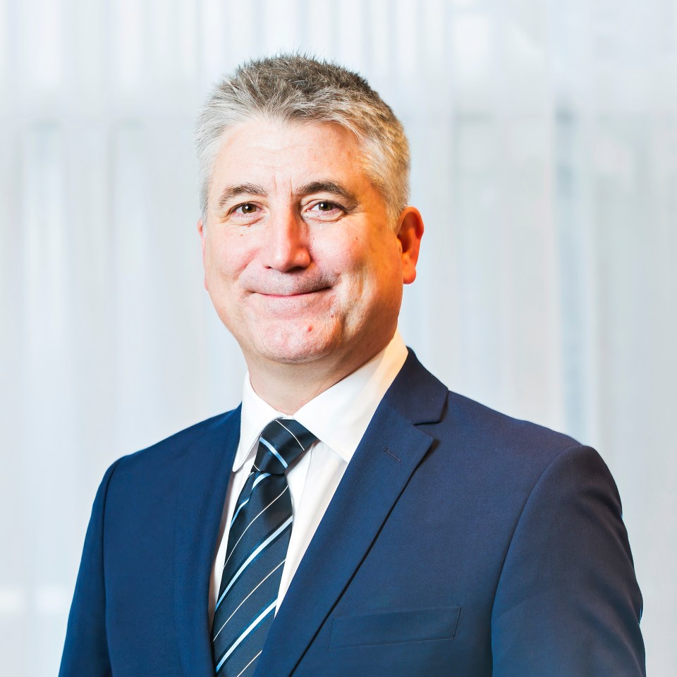 Craig Harrison smiling at a press event, wearing a formal suit, representing his new role in a major business announcement