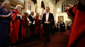 David Cameron speaking at a press conference, wearing a suit and tie, addressing the media with a serious expression.