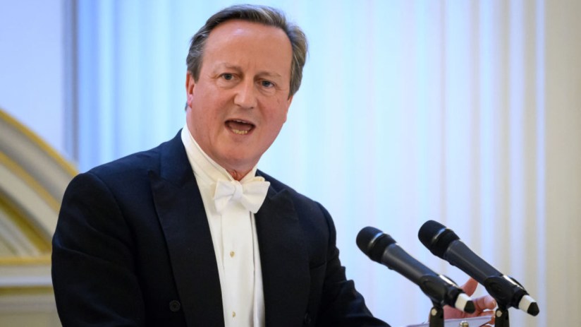 David Cameron speaking at a press conference, addressing political issues and current events, wearing a suit and tie.