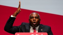David Lammy speaking at a press conference with a focused expression, wearing a suit and tie, addressing key issues.