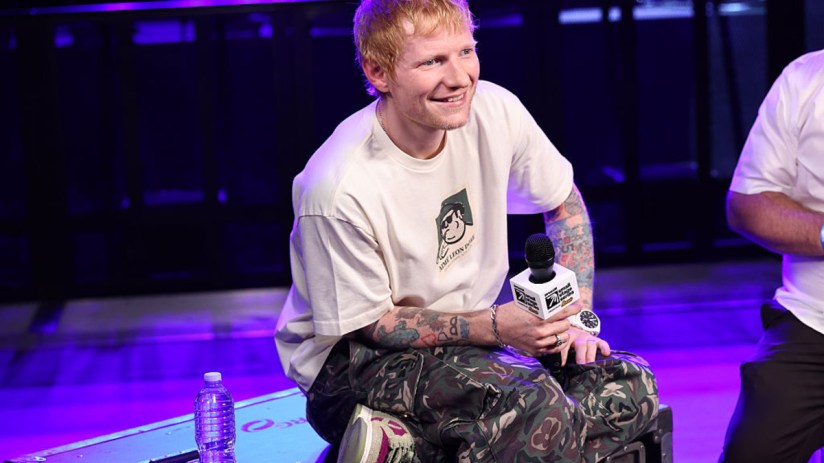 Ed Sheeran performing on stage with a guitar, passionately singing to a large audience at a music event.