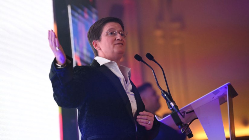 Julia Hoggett speaking at a business conference podium, emphasizing key financial strategies and market insights.