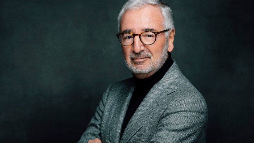 Paul Achleteiner delivering a keynote speech at a business conference, wearing a suit, with a presentation screen in the b...