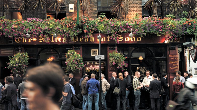 London pub exterior with historic architecture and patrons enjoying drinks on a sunny day, highlighting local social culture.