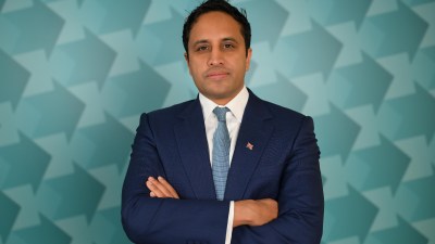 Zia Yusuf at a business event, wearing a suit and tie, delivering a keynote speech in a modern conference setting