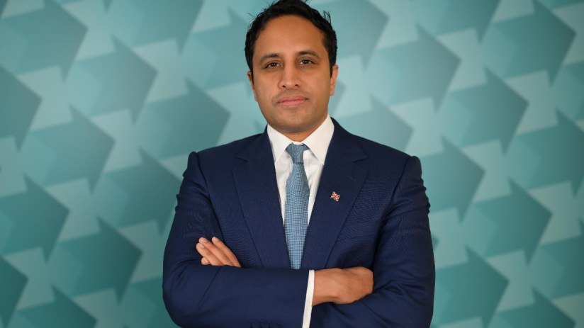 Zia Yusuf at a business event, wearing a suit and tie, delivering a keynote speech in a modern conference setting