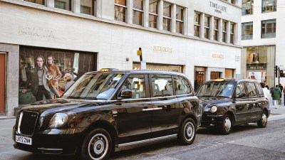 Black cab navigating Bond Street in Mayfair, showcasing Londons iconic taxi service against a backdrop of luxury shops.