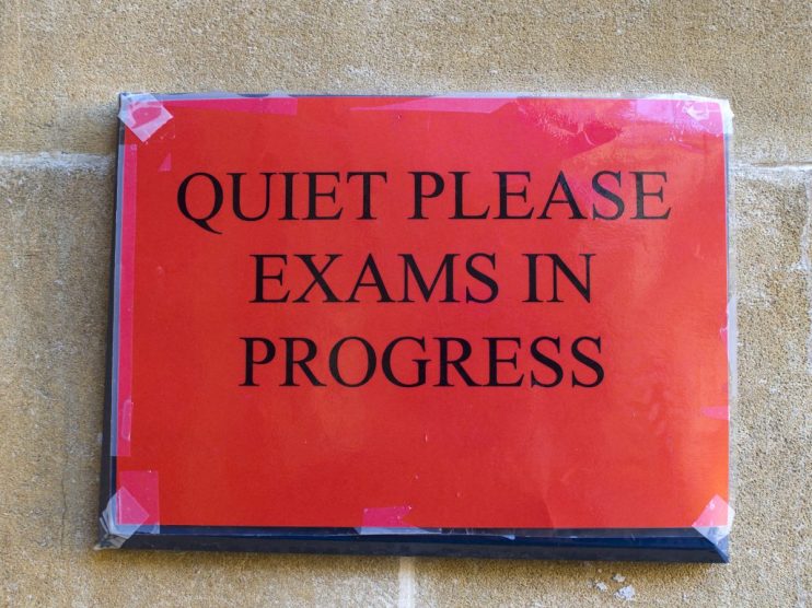 Students attentively taking in-person exams in a large classroom setting, showcasing a return to traditional test environm...