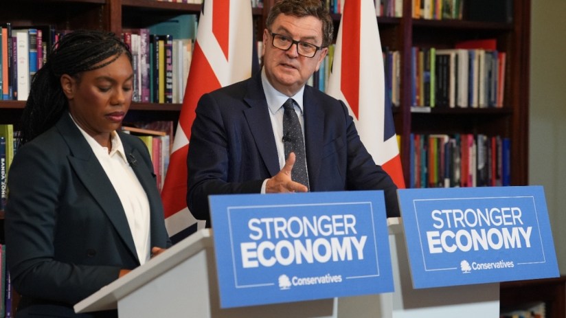 Mel Stride speaking at a press conference, addressing key issues, in a formal setting with a backdrop of the events logo.