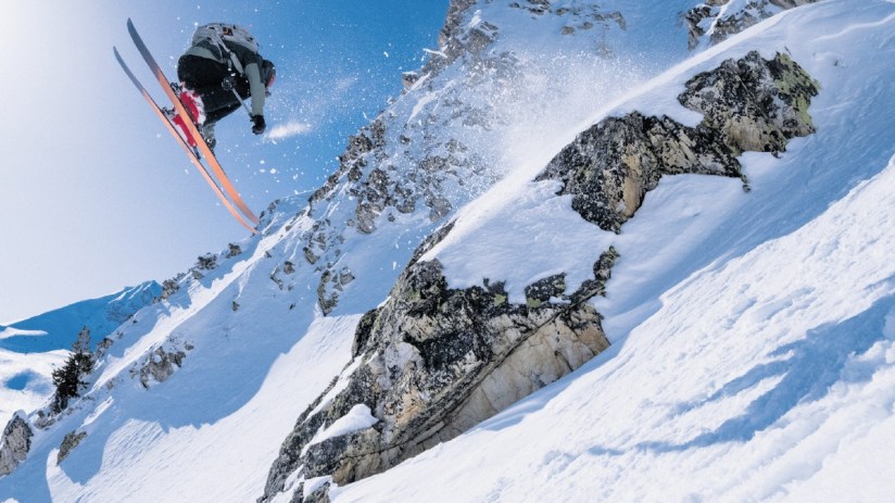 Expert skier carving through fresh powder on a sunny mountain slope, showcasing advanced skiing techniques and winter spor...