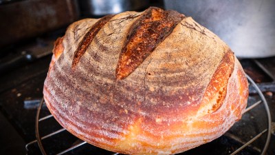 Freshly baked sourdough bread with a golden crust on a wooden board, showcasing artisanal baking techniques.