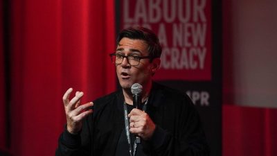 Andy Burnham speaking at a Labour Party event, addressing current political issues, with a focused and determined expression.